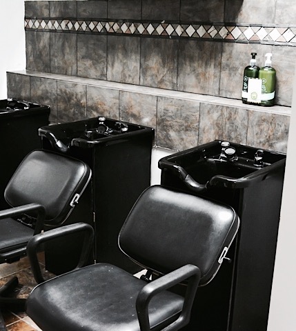 A barber shop with two black chairs and two sinks.